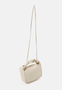 Bolso pequeño de color crema con asa superior retorcida y correa larga para el hombro, mostrado colgando contra un fondo blanco.