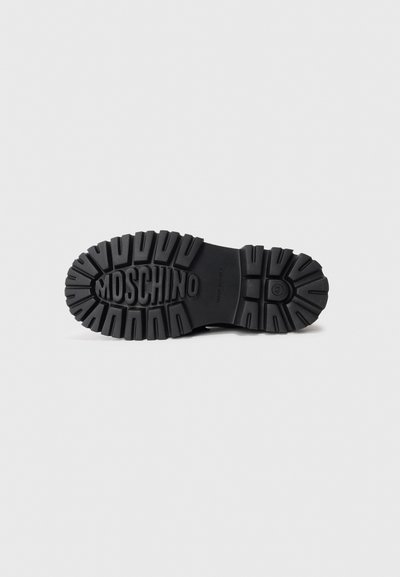 Black rubber boot sole featuring thick tread, embossed logo, and a durable texture designed for traction and stability.