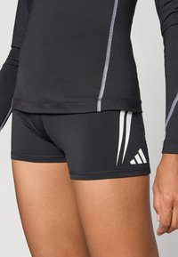 Črne atletske kratke hlače iz raztegljive tkanine, z belimi poudarjenimi črtami in logotipom. Vrh je črn z dolgimi rokavi in kontrastnimi šivi.