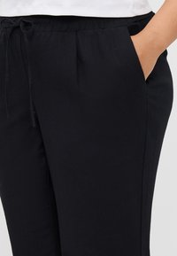 Pantaloni neri leggeri con una vita elastica, cordoncino, tasche laterali e una superficie liscia. Adatti per un abbigliamento casual.