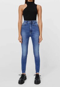 Jean skinny taille haute bleus légèrement décolorés, associés à un haut sans manches noir et des chaussures noires à lacets imposantes.