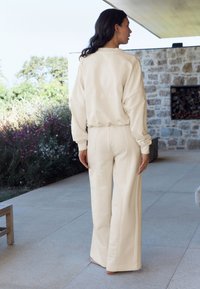 Beige oversized sweatshirt with "b" logo and matching wide-leg trousers, both made of soft fabric, featuring ribbed cuffs and seams.