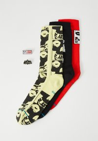 Three pairs of socks: one yellow with black skull pattern, one black, and one red. Includes two pins with skull designs and lettering.