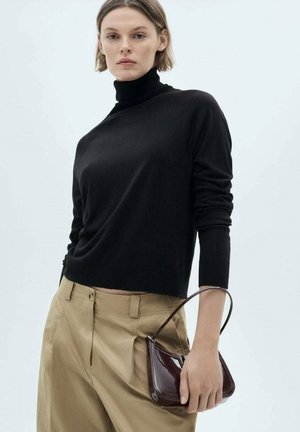 Čierny rolák z jemného úpletu skombinovaný s béžovými nohavicami; modelka drží lesklú bordovú kabelku s zakriveným dizajnom.