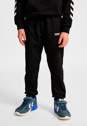 Svarta sweatpants med elastiska muddar och en vit logotyp. Bärs med blå sneakers med en vit design. Materialet verkar mjukt och hållbart.