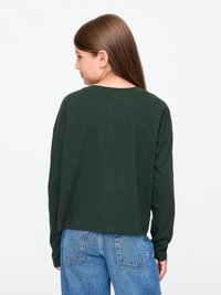 Zöld, hosszú ujjú felső, laza szabással, kerek nyakkivágással és hátul enyhén cropped fazonnal, kék farmerral párosítva.