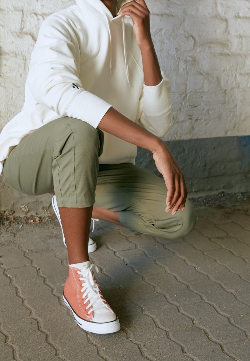 Bílá mikina s kapucí, olivově zelené zkr�ácené kalhoty a oranžové vysoké tenisky s bílými šňůrkami. Strukturované materiály a neformální styl.