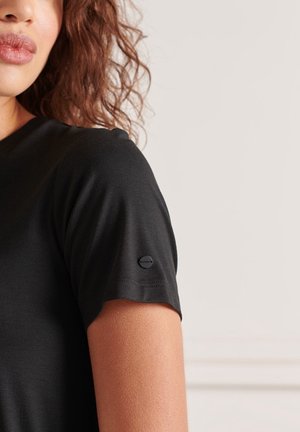 Musta lyhythihainen paita, valmistettu sileästä materiaalista, pyöreällä pääntiellä ja pienellä logotunnisteella vasemmassa hihassa.