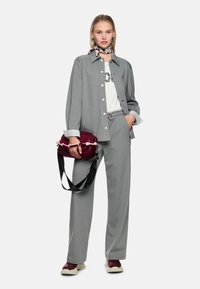 Grauer Nadelstreifen-Hosenanzug mit lockerem Schnitt, kombiniert mit weißem T-Shirt und burgunderroter Handtasche. Strukturierter Schal und sportliche Sneaker.