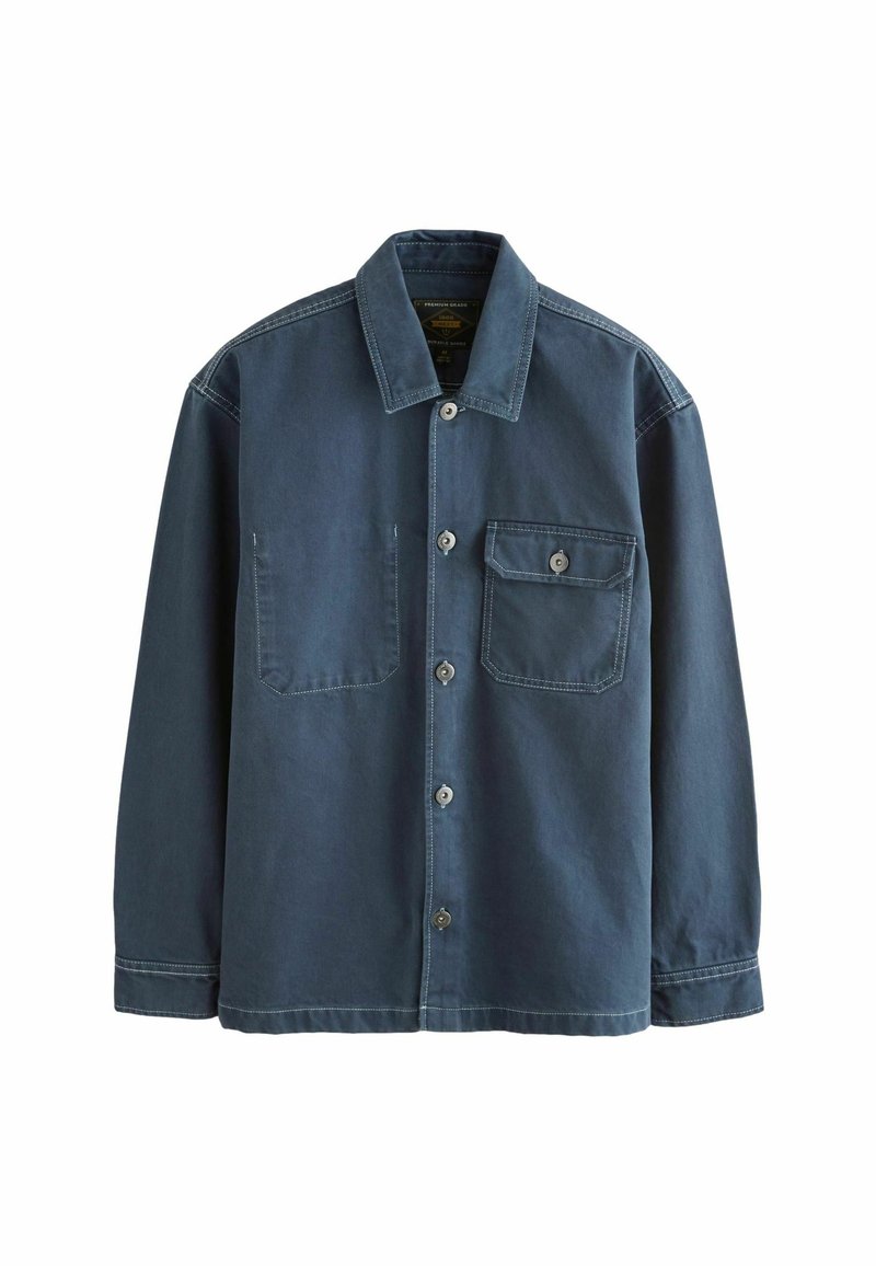 Chemise bleu foncé à manches longues, boutonnée, avec un col pointu et une poche poitrine à bouton sur le côté gauche.