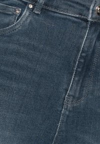Jeans de mezclilla azul oscuro con una textura suave, que presentan bolsillos estándar y detalles de costura, incluyendo un botón de metal y remaches.