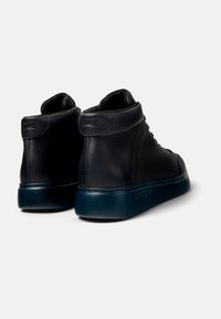 Zapatillas altas de cuero negro con textura suave, puntera redondeada y suela de goma oscura contrastante con el logotipo en la parte trasera.