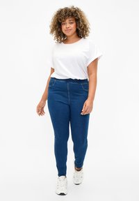 Denim jeggings in dark blue with an elastic waistband and side pockets, paired with a loose-fit white T-shirt. Smooth texture, casual style.