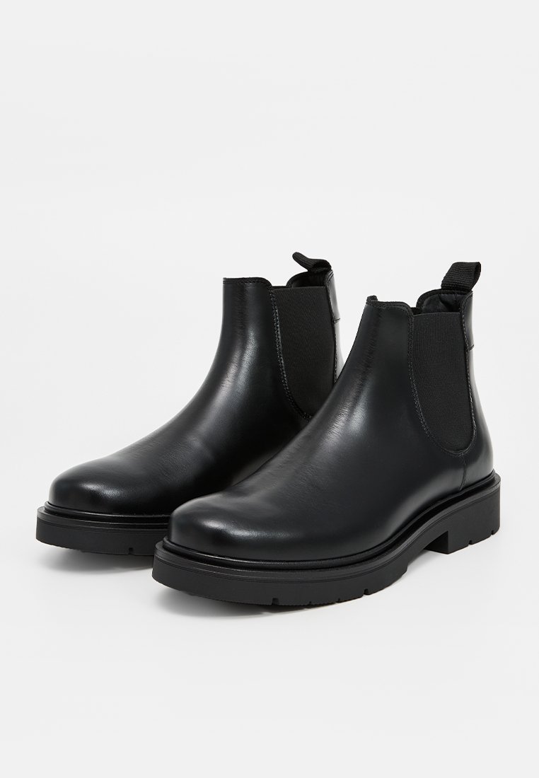 Bottines Chelsea en cuir noir avec des panneaux latéraux élastiques, un bout arrondi et une semelle en caoutchouc texturée. Convient pour un usage décontracté ou formel.