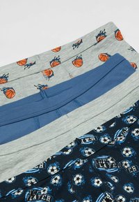 Trois paires de sous-vêtements pour garçons : gris avec des imprimés de basket-ball, bleu de couleur unie et marine avec des graphismes et du texte sur le soccer.