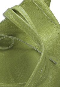 Close-up van een lege lichtgroene leren handtas die de textuur van het oppervlak, de stikdetails en de open bovenkant toont.