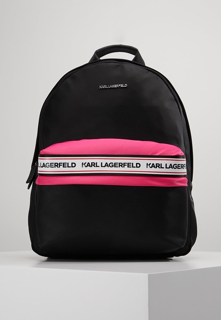 Sac à dos noir avec poche avant rose, sangle blanche avec le texte répété "KARL LAGERFELD", et petite anse sur le dessus.