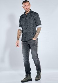 Schwarz-weiß gestreiftes Hemd mit Knöpfen, kurzen Ärmeln, kombiniert mit grauen Jeans und grünen Schnürstiefeln, mit schlank geschnittenem Design.