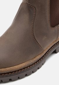 Braune Leder-Ankle-Boots mit elastischen seitlichen Einsätzen, robustem Gummisohle und sichtbarem Nähdetail. Glatte Textur mit einem abgenutzten Finish.