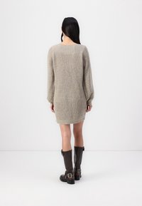 Vestito a maglia color beige chiaro con maniche lunghe a costine e silhouette dritta, abbinato a stivali alti in pelle marrone scuro.