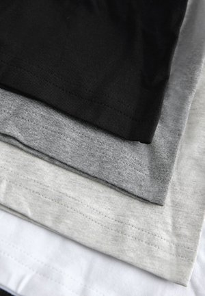 Fire t-shirts stablet: sort, mørkegrå, lysegrå og hvid. Alle er bomuld med en glat tekstur og synlige syninger på kanterne.