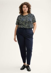 Short-sleeve navy top with a colorful polka dot pattern, paired with navy fitted pants and black lace-up shoes.