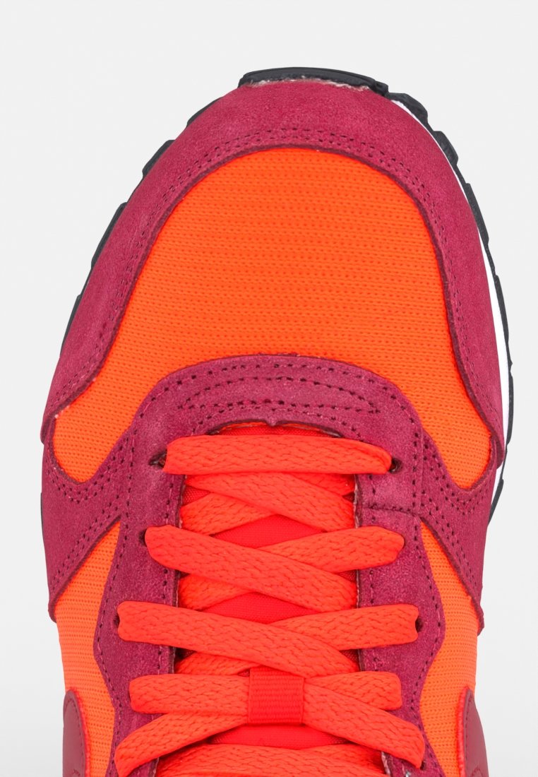 Zapatilla deportiva en un brillante naranja y rojo intenso, con texturas de malla y ante, cordones planos y una suela de goma negra.