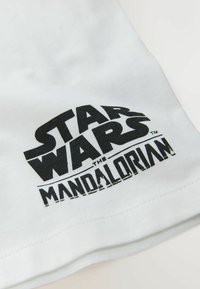 T-shirt en coton blanc avec un imprimé graphique noir portant le texte "STAR WARS THE MANDALORIAN" et une illustration en dessous.