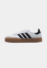 White Adidas Samba sneaker with black stripes, gum sole, grey suede toe cap, and gold "SAMBA" text on side.