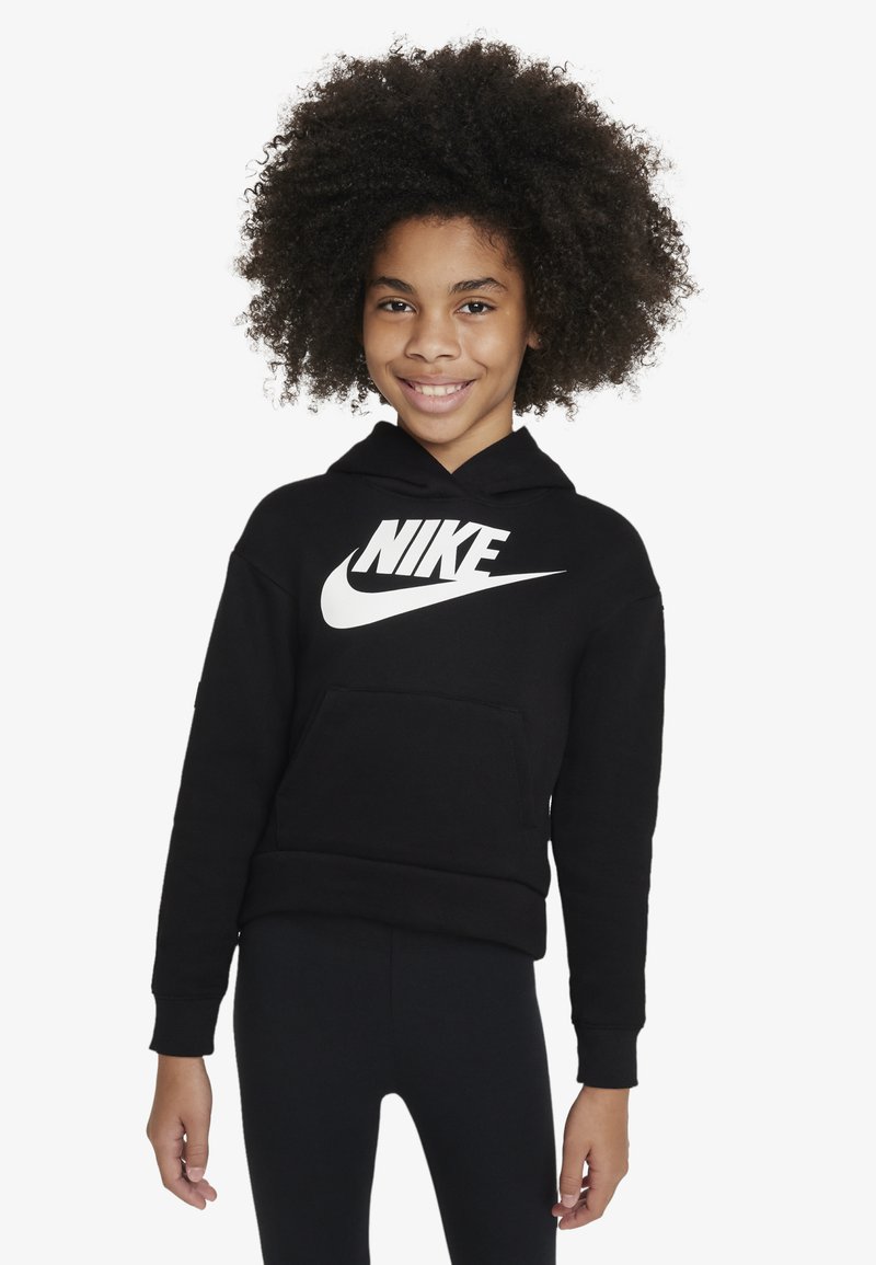 Black Nike hoodie with a white logo, front pocket, and a hood. The fabric appears soft and textured. Worn with black leggings, hands visible.