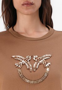 Brown sweatshirt met een decoratieve versiering van heldere en roségouden stenen, gerangschikt in een symmetrisch, bloemig ontwerp.