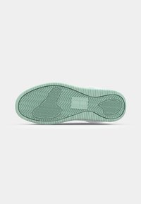 Semelle d'une sneaker verte claire avec un motif de grip texturé et le logo "Tommy Jeans" au centre.