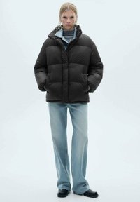 Sort pufferjakke med høj krave, quiltet design og lynlås. Parret med lyseblå vide jeans og sorte sko.