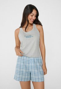 Canottiera grigia con scritte blu, abbinata a pantaloni corti a quadri blu con chiusura a bottoni e una vestibilità comoda. I materiali sembrano soffici e leggeri.