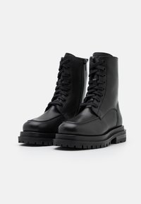 Bottes noires en cuir à la cheville avec un bout rond, ouverture à lacets, fermeture éclair latérale et semelle en caoutchouc robuste. Caractéristiques : texture lisse et design solide.