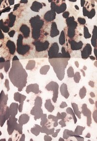 Tissu imprimé léopard avec de grandes taches noires et brunes sur un fond beige, avec un tissage fin et texturé.