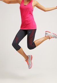 Top deportivo rosa y leggings capri negros con acentos rojos. Las zapatillas para correr cuentan con malla gris y acentos en naranja y verde neón.