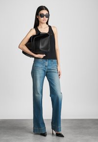 Camisola preta, jeans de ganga azul de cintura alta com um corte descontraído, mala estruturada preta, sapatos de salto baixo e óculos de sol.