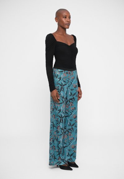 Μαύρη ρυαριστή μπλούζα με μακριά μανίκια σε συνδυασμό με τουρκουάζ παντελόνι σε φαρδιά γραμμή που έχει λουλουδάτα μοτίβα σε κόκκινο και μαύρο. Μαύρα παπούτσια συμπληρώνουν το σύνολο.