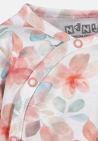 Blommönstrad ekologisk bomullstop med mjuka pastellfärger, med tryckknappslås och rund halsringning. Designen inkluderar rosa och blå accenter.