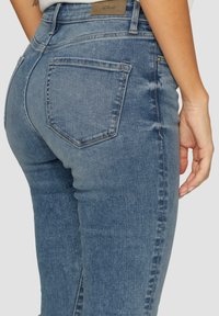 Modré džíny z denimovej látky s priliehavým strihom, stredne vysokým pásom, päť vreckami a logom na zadnom páse. Hladká textúra.