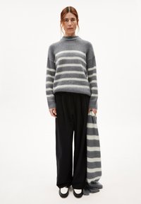 Grau gestreifter Pullover aus weichem Material mit hohem Kragen. Lockere schwarze Hose und ein passender grau gestreifter Schal.
