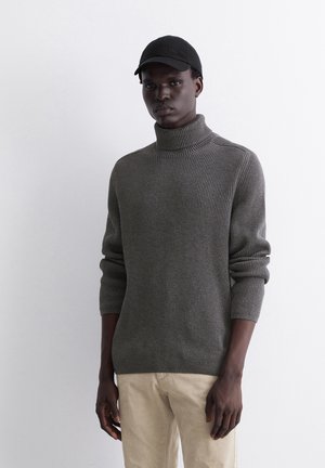 Grau gerippter Rollkragenpullover mit langen Ärmeln, aus Strickmaterial, kombiniert mit hellen Hosen und einer schwarzen Kappe.