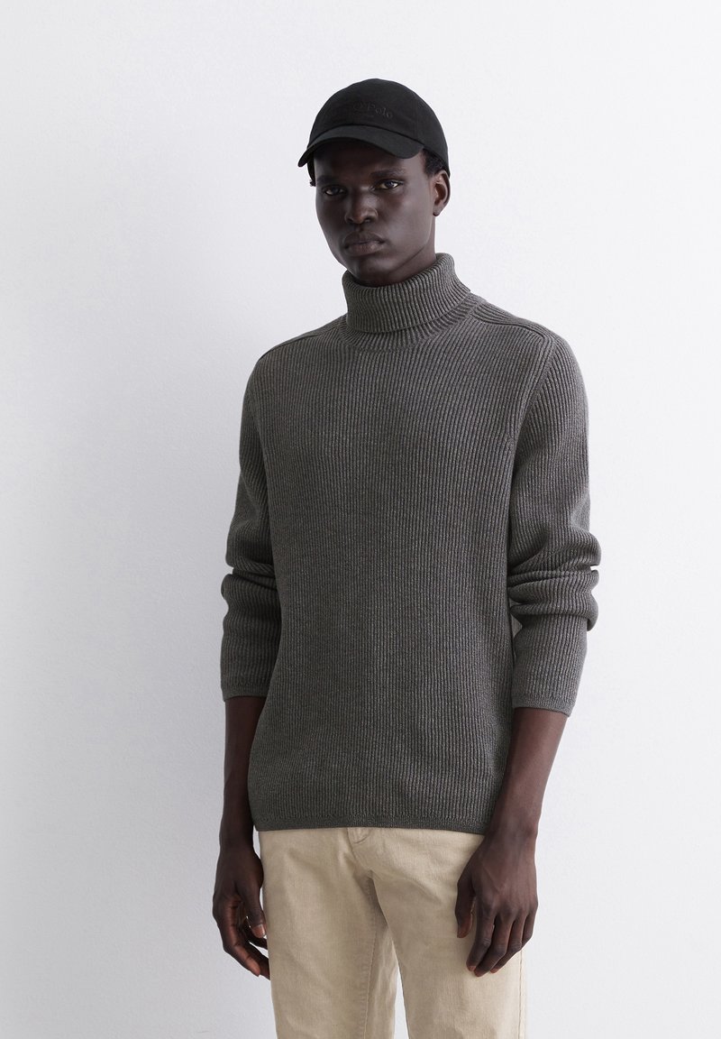 Grau gerippter Rollkragenpullover mit langen Ärmeln, aus Strickmaterial, kombiniert mit hellen Hosen und einer schwarzen Kappe.