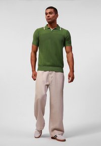 Zöld rövid ujjú póló texturált kötött mintával és fehér gallérral, bézs bő szárú nadrággal és fehér tornacipővel párosítva.