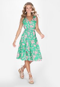 Rochie florală verde cu modele roz, decolteu în v, talie ajustată, fustă evazată, confecționată dintr-un material ușor; asortată cu espadrile bej cu bretele.