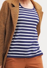 Brown textured cardigan layered over a navy and white striped shirt. The shirt has a round neckline and short sleeves. Brown trousers complete the look.