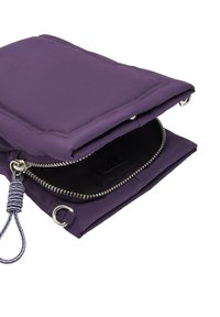 Fioletowa miękka torba otwiera się, aby ujawnić czarne wnętrze z zamkiem błyskawicznym. Posiada boczny pasek o teksturze oraz akcent w postaci pierścienia.