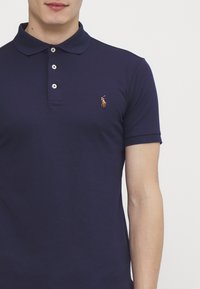 Granatowa koszulka polo wykonana z miękkiej bawełny, z klasycznym kołnierzykiem, pięcioma guzikami i małym haftowanym logo po lewej stronie klatki piersiowej.