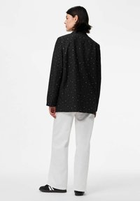 Juodas švarkas su baltomis taškeliais, priderintas pagal figūrą, klasikiniai atvartai, derinamas su baltais tiesiais džinsais ir juodais sportbačiais.